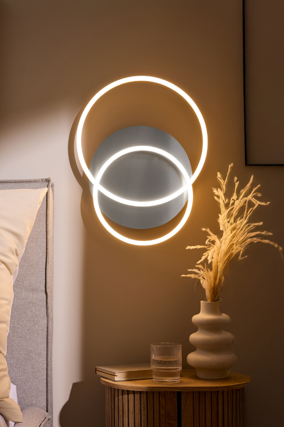 Φωτιστικό τοίχου με δύο φωτιζόμενους κύκλους πάνω από κομοδίνο με διακοσμητικά.